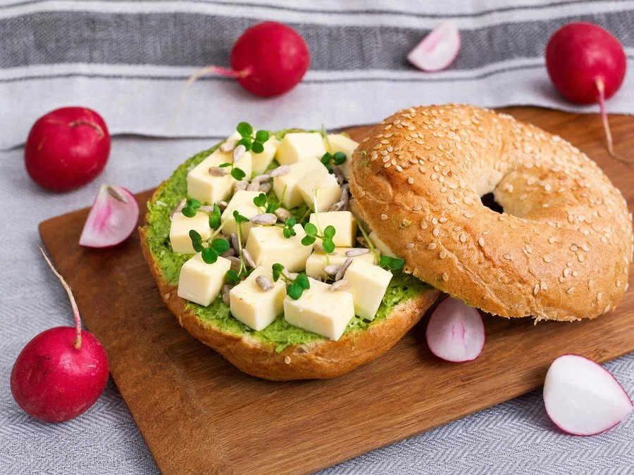 A sesame bagel with chive butter, gouda and microgreens